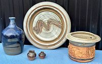 Photo showing all six pottery pieces including a large blue bottle vase, two small brown vases, a decorative plate with an abstract squiggle design, and a lidded bowl with textured relief.