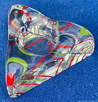 Triangular clear glass votive candle holder with red and green swirled decoration viewed from above on a blue background.