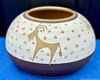 Full side view of the rounded Navajo pottery bowl showing cream upper section with brown stylized goats and small decorative spots, and the solid dark brown bottom section