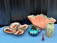 Full view of the vintage pottery lot including the coral pink pitcher, turquoise and blue small pitcher, two vases, and the four-petal decorative plate with red abstract patterns.
