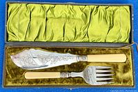 Fish serving knife and fork resting in original box lined with green satin and velvet