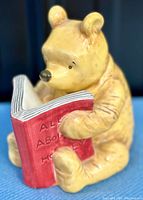 Front close-up of the ceramic Winnie the Pooh bank holding red book