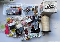 Overview of assorted fly fishing thread spools and packets in various colors and brands laid out on table