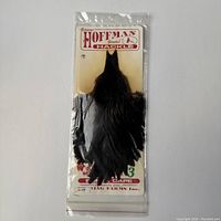 Front view of the black feather cape, packaged with Hoffman Genuine Hackle branding visible.