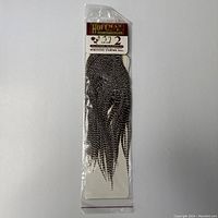 Full view of the sealed plastic pack containing grizzly saddle hackle feathers with Hoffman label