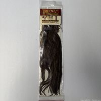 Full view of the Hoffman Genetics dry fly hackle feather pack, showing dark brown saddle feathers inside sealed plastic bag with label on top.