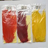 Three packs of dyed over white saddle feathers in orange, red, and yellow colors for fly fishing fly tying.