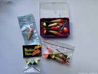 Photo showing various fishing floats of different sizes in plastic container, bag, and packages.