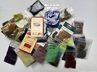 Photo showing multiple small sealed resealable plastic bags with dubbing fibers in a wide range of colors including greens, blacks, purples, orange, cream, and brown, some with original brand packaging and printed labels.