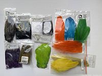 Assortment of packaged and loose dyed and natural feathers for fly tying, including orange, blue, green, yellow, chartreuse, and purple hackle feathers