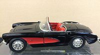 Side profile of black and red 1957 Chevrolet Corvette model car showing convertible body style and detailed wheels.