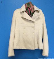 Front view of cream alpaca wool jacket with double-breasted buttons and striped scarf on collar against blue background.