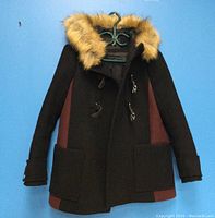 Front view of the MAJE ladies' wool jacket showing black and brown color panels, toggle closures, faux fur hood and large front pockets.