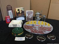 Full lot overview showing all items including books, ashtrays, beer stein, Man Cave sign, thermometer, and coasters