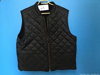 Front view of black men's heavy duty vest on yellow hanger against blue background.