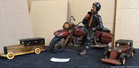 Photo showing the motorcycle and rider figurine alongside two wooden model cars, one longer with a black roof and one with a red body.