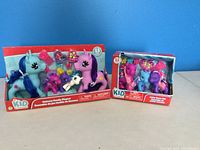 Front view of new boxed Unicorn Family Playset with large blue and pink unicorns and smaller horse figures next to boxed Little Horse Set containing three small horses and accessories