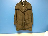 Front view of the army green Ralph Lauren ladies winter coat hanging against a blue wall.