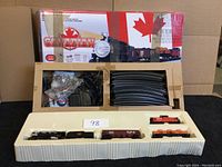 Full boxed train set with molded insert showing train cars, tracks, and power supply. Box top shows Canadian theming and train image.