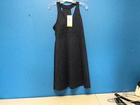 Full view of the dark grey sleeveless dress with built-in bra liner hanging on a clear plastic hanger against a blue wall.