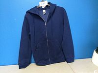 Front view of the navy blue zipped hoodie hanging on a hanger against a blue background showing full zip and kangaroo pocket.