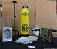 Full view of lot displaying the yellow aqua-lung vintage divers tank, R.C.S.C.C. Renown sailor hat, model ship, book, photograph, candle holder and lantern stand.