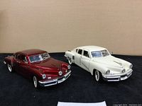 Two 1948 Tucker model cars side-by-side, white and red, showing front and side details.