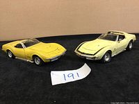 Two vintage Corvette model cars, one yellow convertible and one cream hardtop with T-tops, shown side by side.
