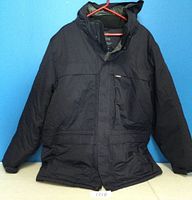Front view of black Wind River T-Max parka jacket hanging showing front zip closure, hood, and multiple pockets.