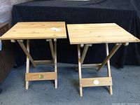 Front view of two solid wood pop-up end tables with tops raised, showing fold-down legs and brass medallions on front support boards.