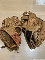 Two vintage MacGregor baseball gloves side by side, showcasing overall wear and branding on wrist strap areas.