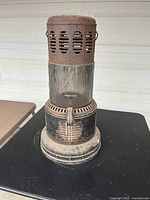 Front view of antique rusted metal kerosene gas heater with glass globe section showing flame design.