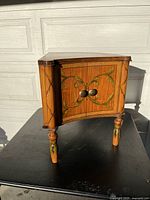 Front view of three-sided cabinet showing wooden construction, green painted decoration, and round knobs.