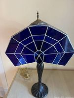 Front view of the Art Deco style lamp showing twisted bronze-colored base and cobalt blue web pattern shade