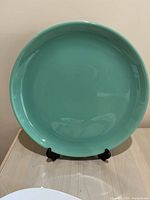 Front view of large round foam green ceramic dish on a black stand.