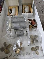 Various Marx brand hobby gear units, some sealed in plastic packaging, others in original boxes, and several small RC boat propellers made of brass or metal.