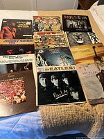 Photo showing a selection of vintage vinyl records including Jackie Wilson, The Jimmy Smith Trio, The Beatles, Faces, and others on a bed surface.