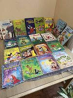 Overall view of 20 vintage Disney children's books displayed on floor and table showing colorful covers and titles.