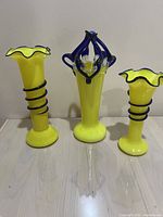 Front view of three art glass vases side by side showing bright yellow glass and cobalt blue accents.
