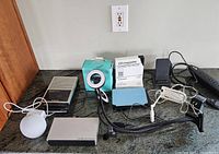 Photo showing various tech gadgets including the vintage voice recorder, turquoise video conference light, Kindle, and multiple cables.