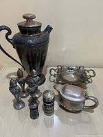 Overview photo showing all items in the lot: Wilcox decanter, U.S. Navy creamer, four salt and pepper shakers, and small footed dish placed on a white surface against a plain wall.