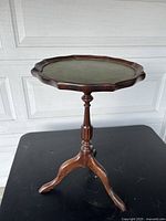 Full view of small round wooden accent table with faux leather top, showing the tripod pedestal base and carved edge.