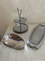 Two-tiered tray with brass handle alongside two flat trays on table, showing polished chrome finish and shapes