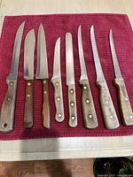 All 8 vintage kitchen knives arranged on a burgundy towel to show wooden handles and blades.