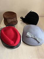 Four vintage women's designer hats in various materials including velour, felt, and wool, arranged on a surface.