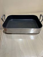 Full front view of the rectangular aluminum roasting pan showing the black non-stick interior and metal handles.