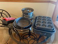 Photo showing assortment of bakeware including metal mixing bowl, bundt pans, springform pan, muffin pans, baking sheets, and silicone mitts.