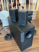 Photo of Bose Acoustimass 5 Series II system showing subwoofer and two satellite speakers on top with wires visible.