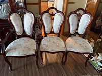 View of six mahogany dining chairs, two with armrests (captains chairs) and four armless side chairs, all with matching floral upholstery.