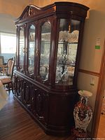 Wood china cabinet with glass doors, mirror back, showing contents inside including glassware and decorative items